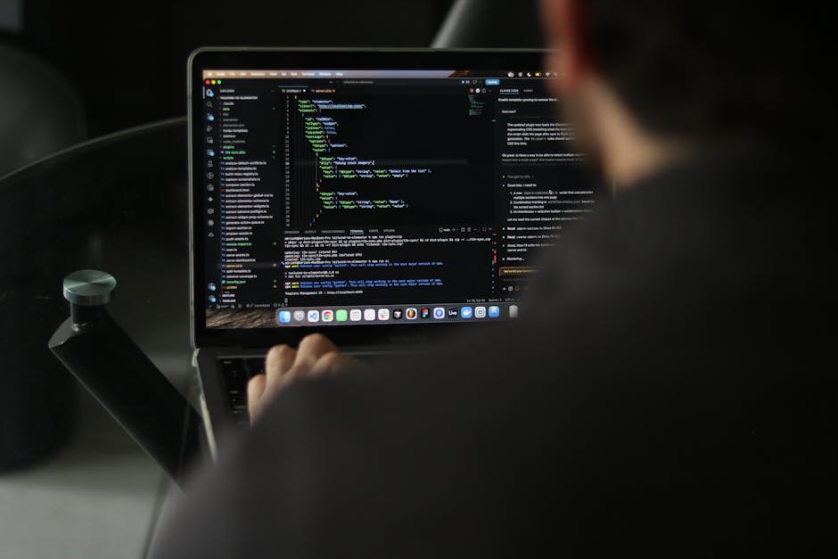 A close-up view of a laptop screen displaying lines of colorful code on a dark background, with a blurred dark environment in the background. The code includes various syntax elements highlighted in m