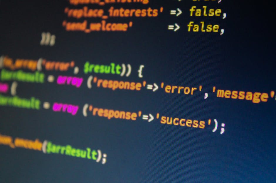 The image displays a close-up of a computer screen with lines of colorful programming code in various colors including orange, pink, green, and yellow on a dark background. The code appears to be Java
